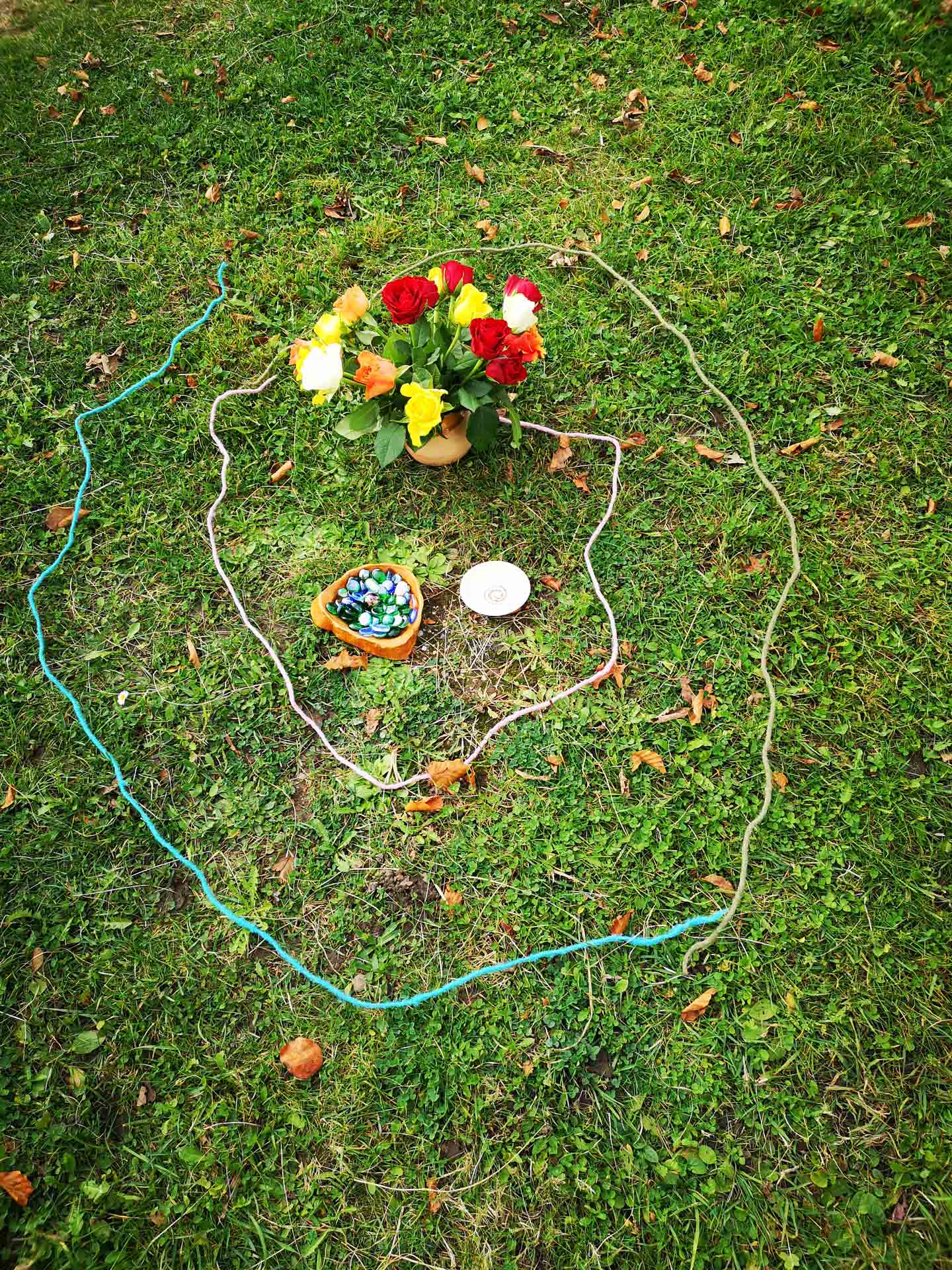 Dekoration aus farbigen Seilen, Blumenstrauß und Steinen/Muscheln auf einer grünen Rasenfläche.