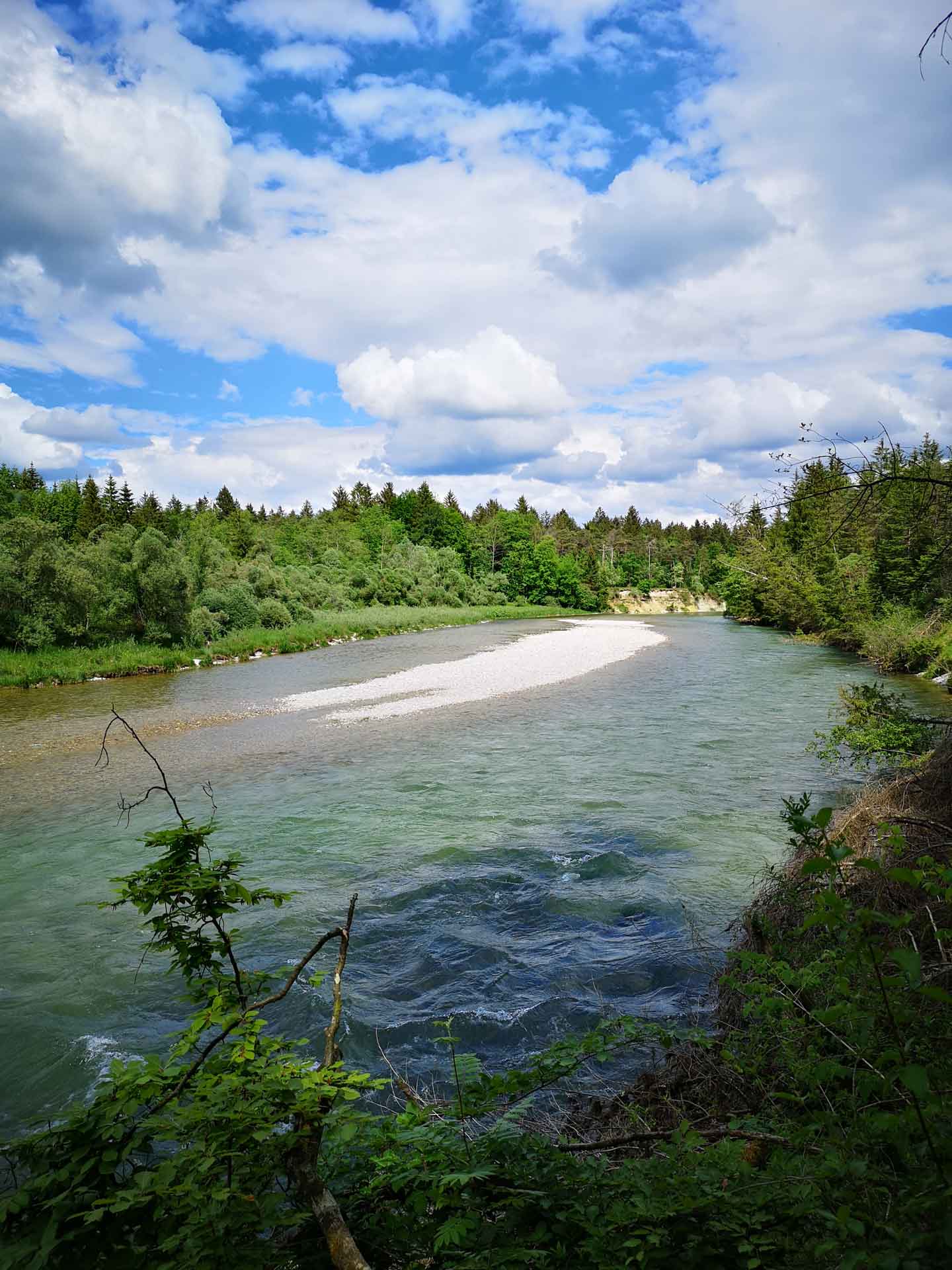 Flussbiegung mit türkisfarbenem Wasser und großer, heller Schotterbank vor einem grünen Steilhang.