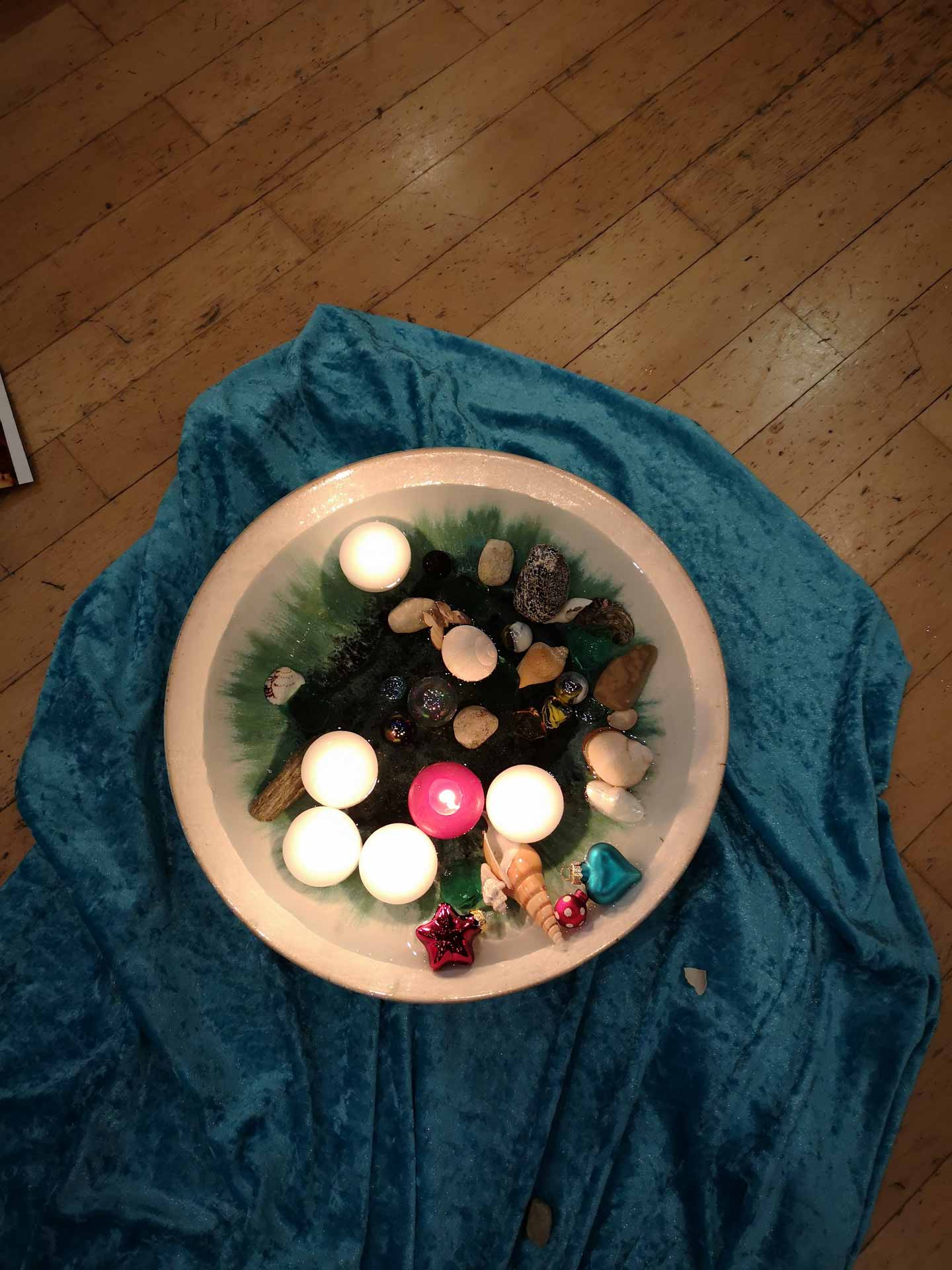 Flache Schale mit drei weißen und einer pinken Schwimmkerze, umgeben von Muscheln und Dekosteinen bei unserem Trauercafé.