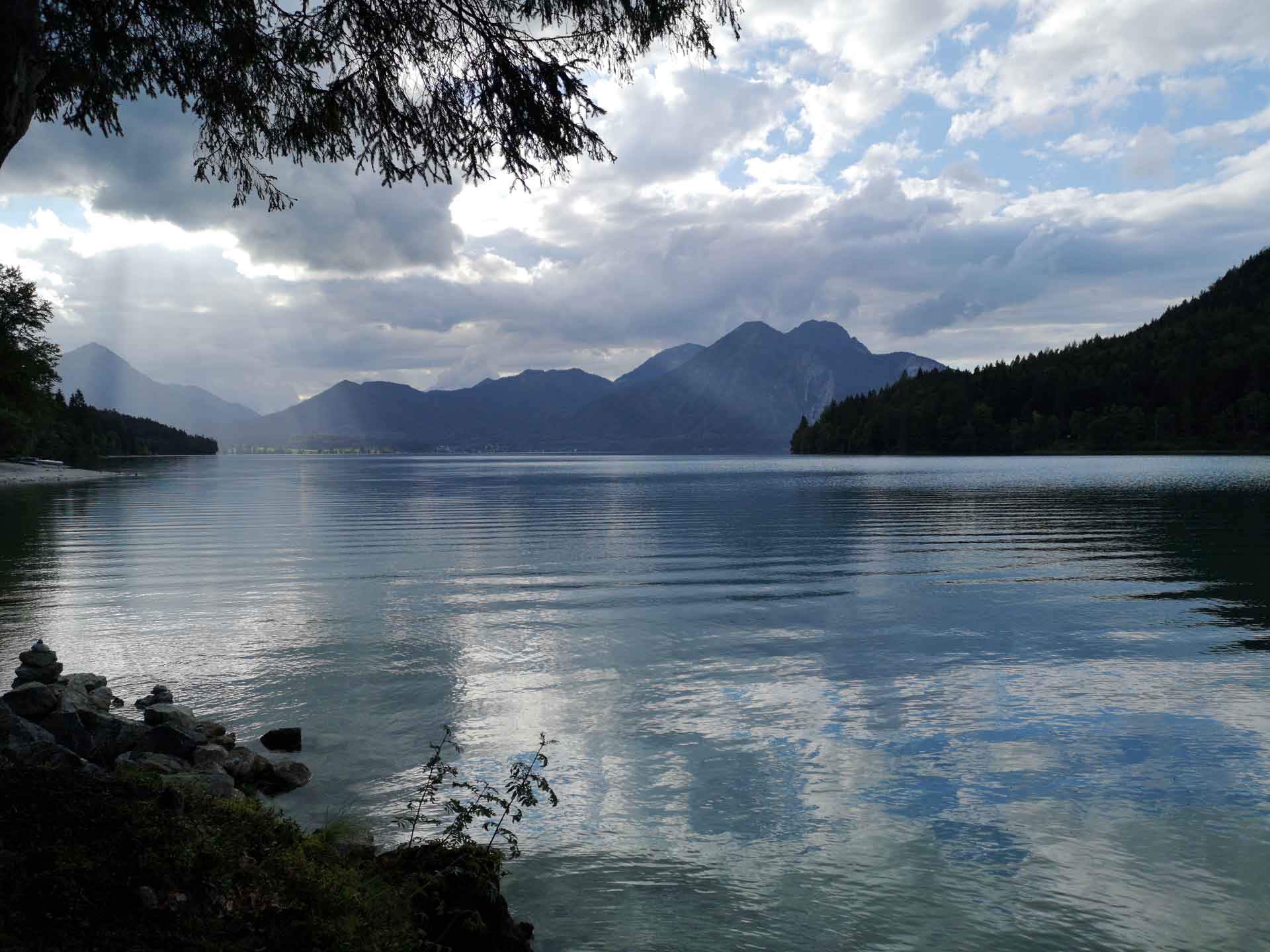 Gebirgssee (Walchensee) mit dunklen Wolken, die sich im Wasser spiegeln, umgeben von bewaldeten Bergen.