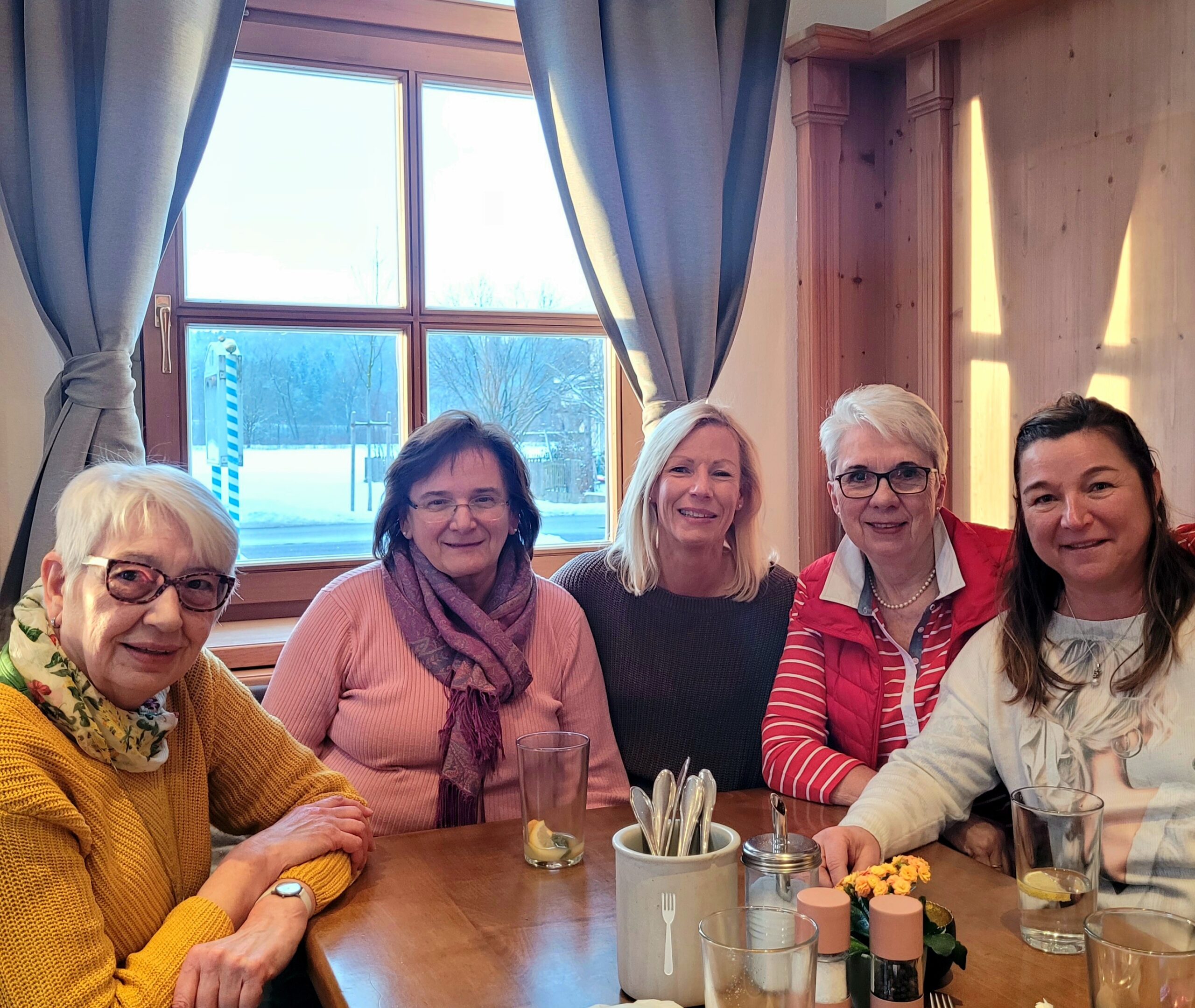 Fünf lächelnde Frauen sitzen bei gemütlichem Beisammensein an einem Holztisch im traditionellen Wirtshaus.