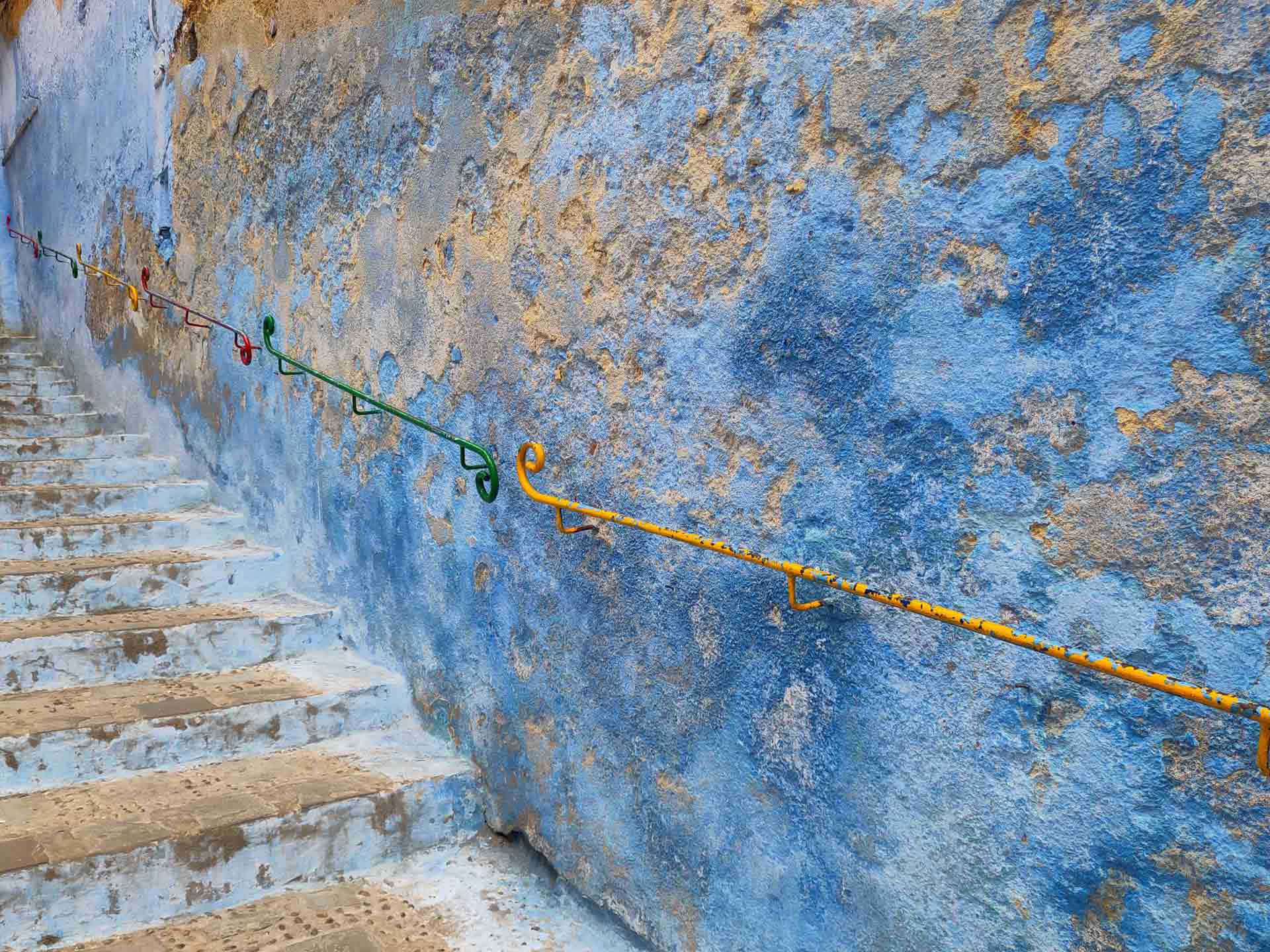 Treppe vor blauer Außenwand mit buntem Geländer